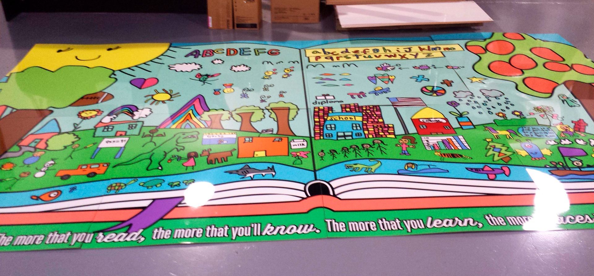 Colorful illustration of an open book with a whimsical town scene. Includes a smiling sun, trees, and buildings.