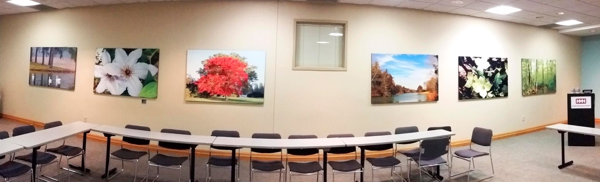 Conference room with long tables arranged in a U-shape, decorated with landscape paintings.
