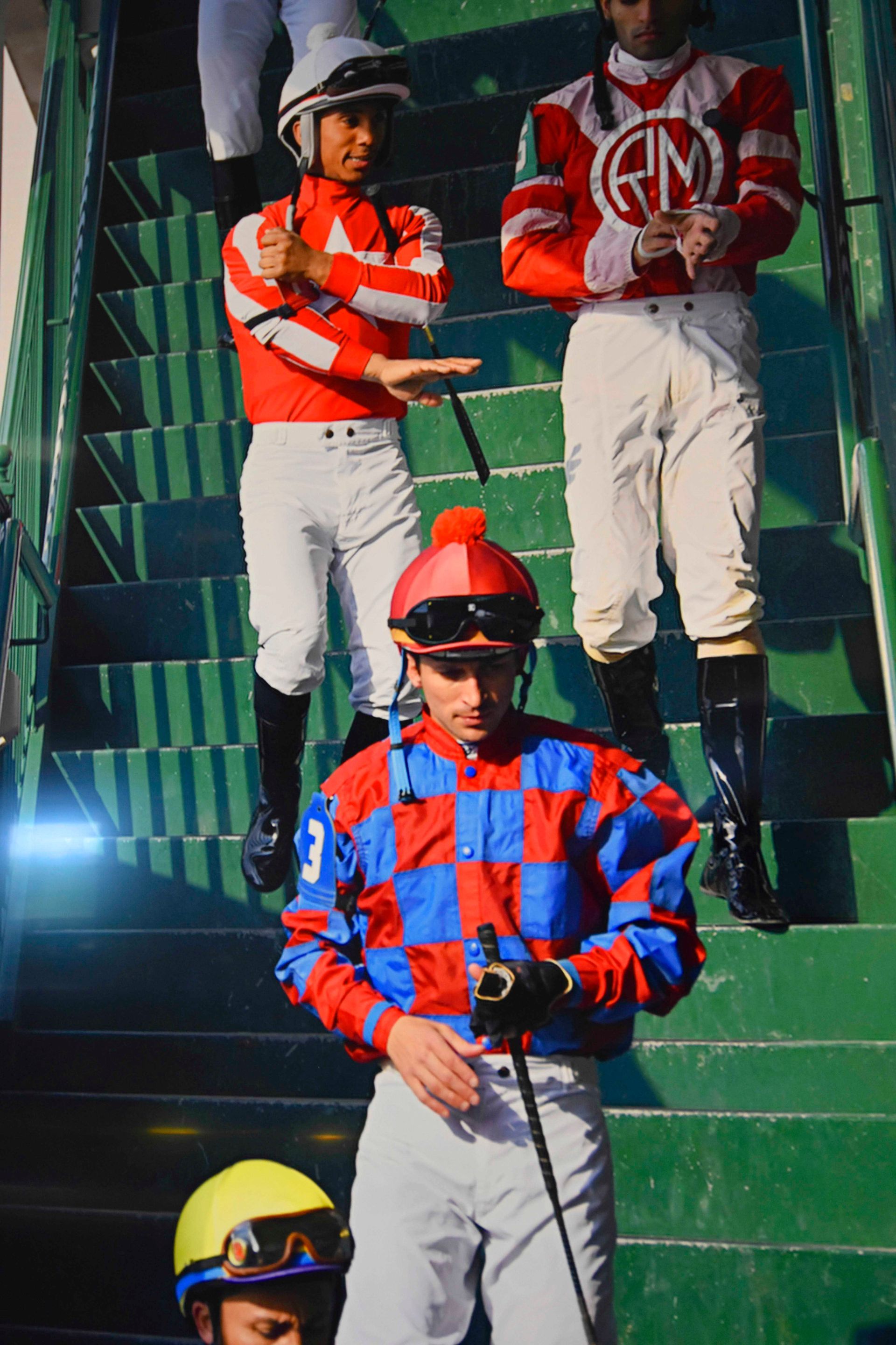 Jockeys in colorful silks on stairs, holding riding crops.