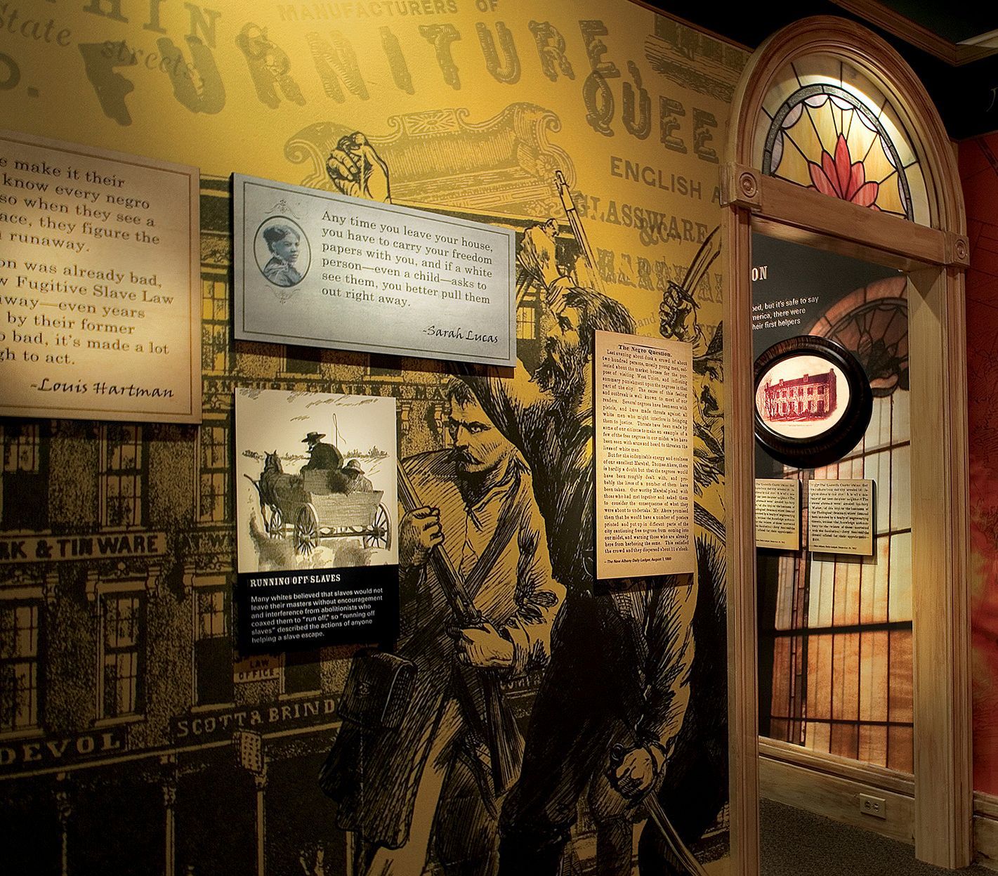 Museum display: Historical documents, illustrations, and an arched doorway leading to another exhibit.