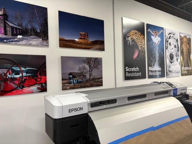 Large format printer with mounted photos and posters showcasing scratch resistance.