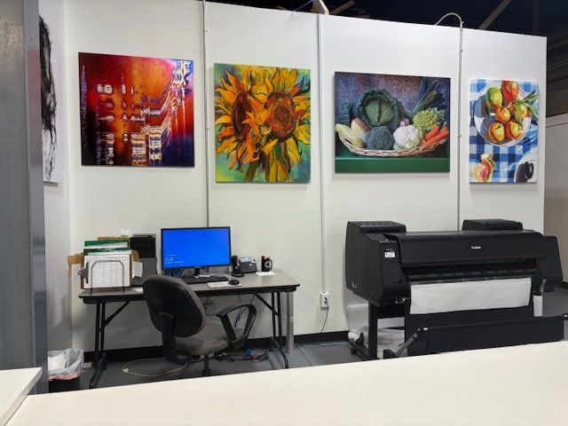 Office with paintings on the wall. Desk with computer and printer. Artwork includes a sunflower and fruit.