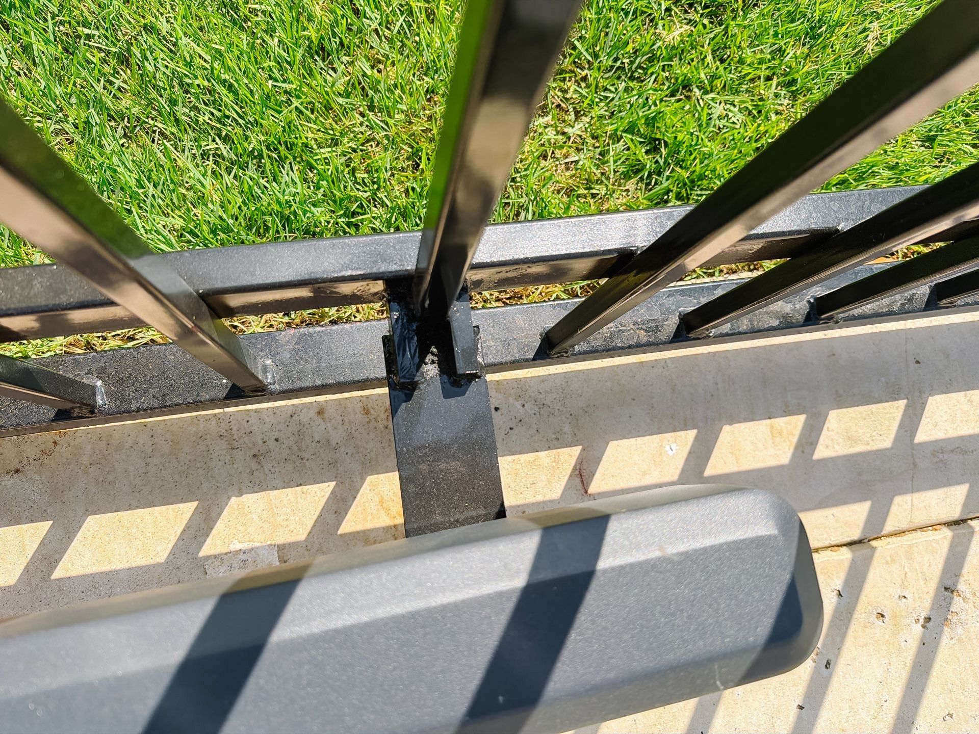 Black metal fence beside a green lawn, with a sidewalk edge and shadowed steps in the foreground