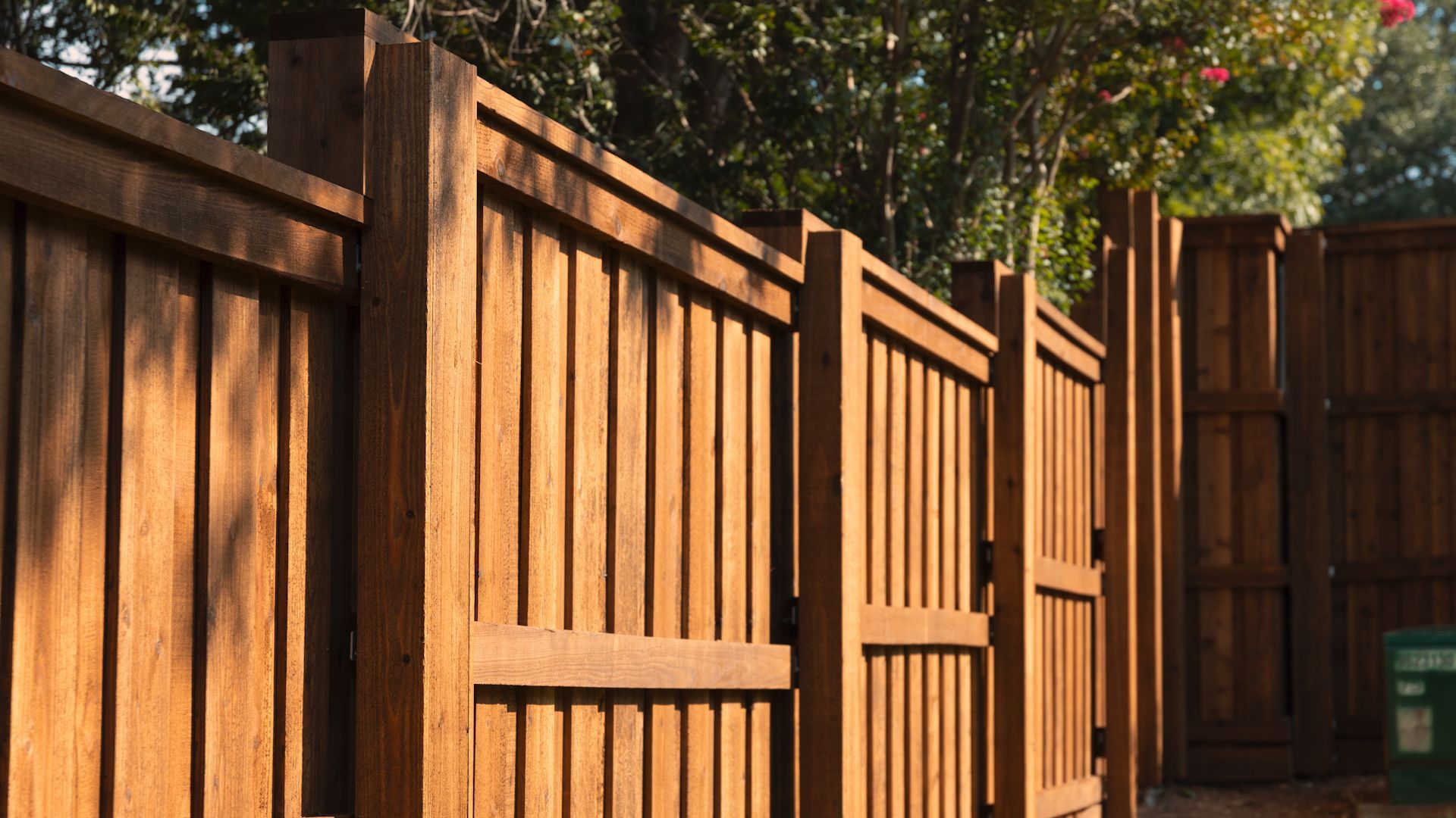 Wooden fence with vertical planks, stained brown, in a sunny outdoor setting.
