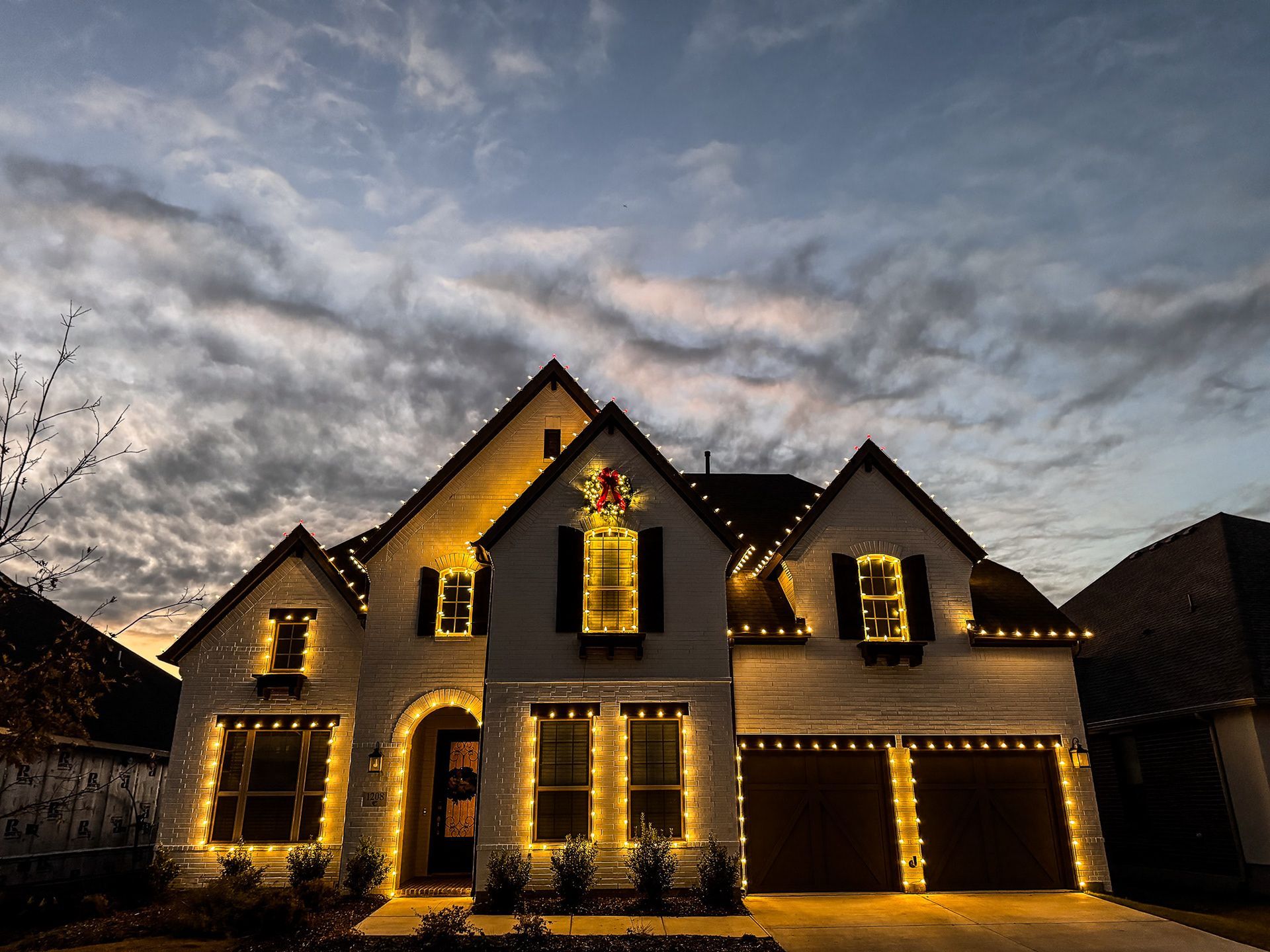 House decorated with yellow Christmas lights against a cloudy evening sky.