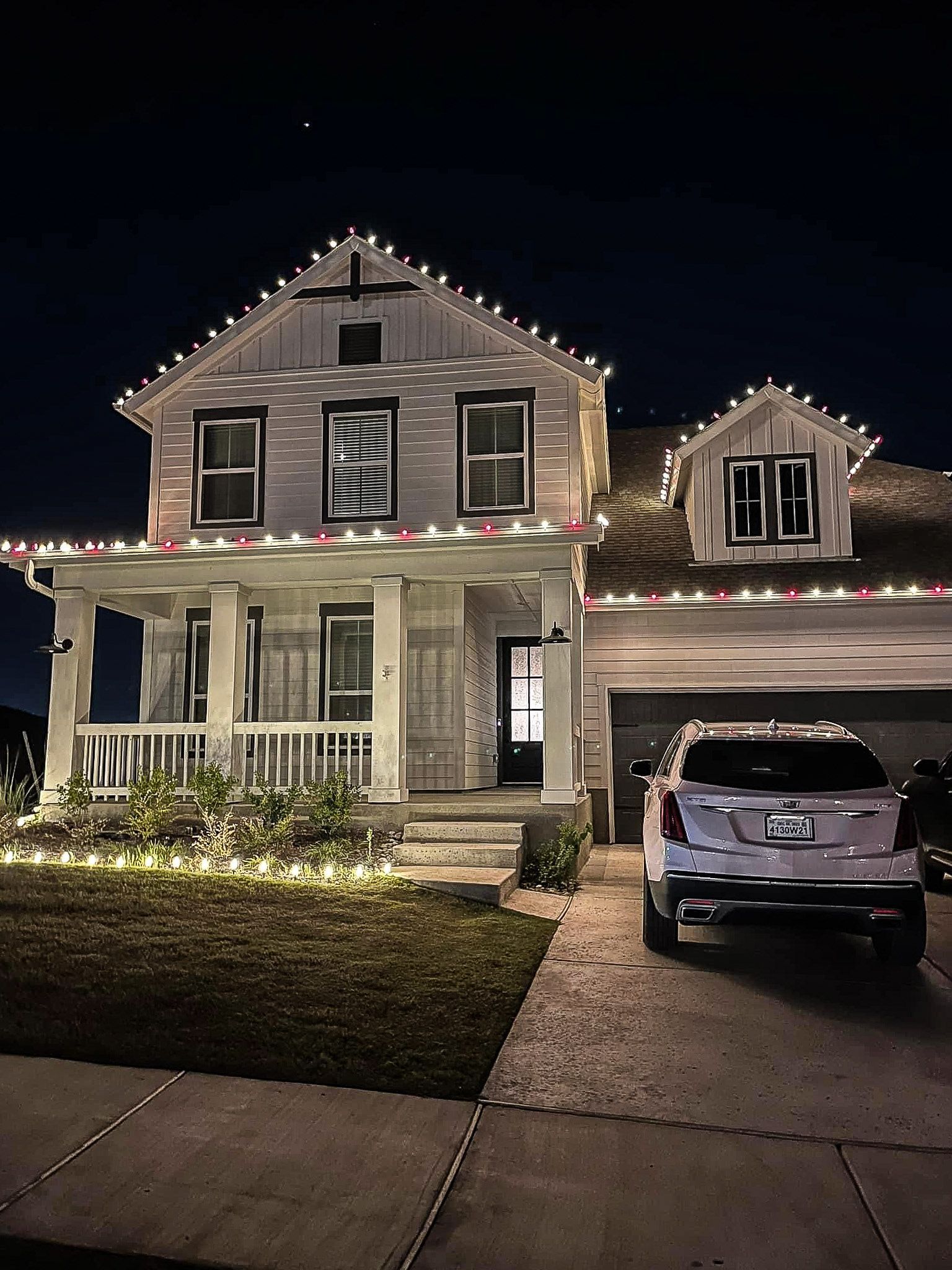 House decorated with Christmas lights at night, car in driveway.