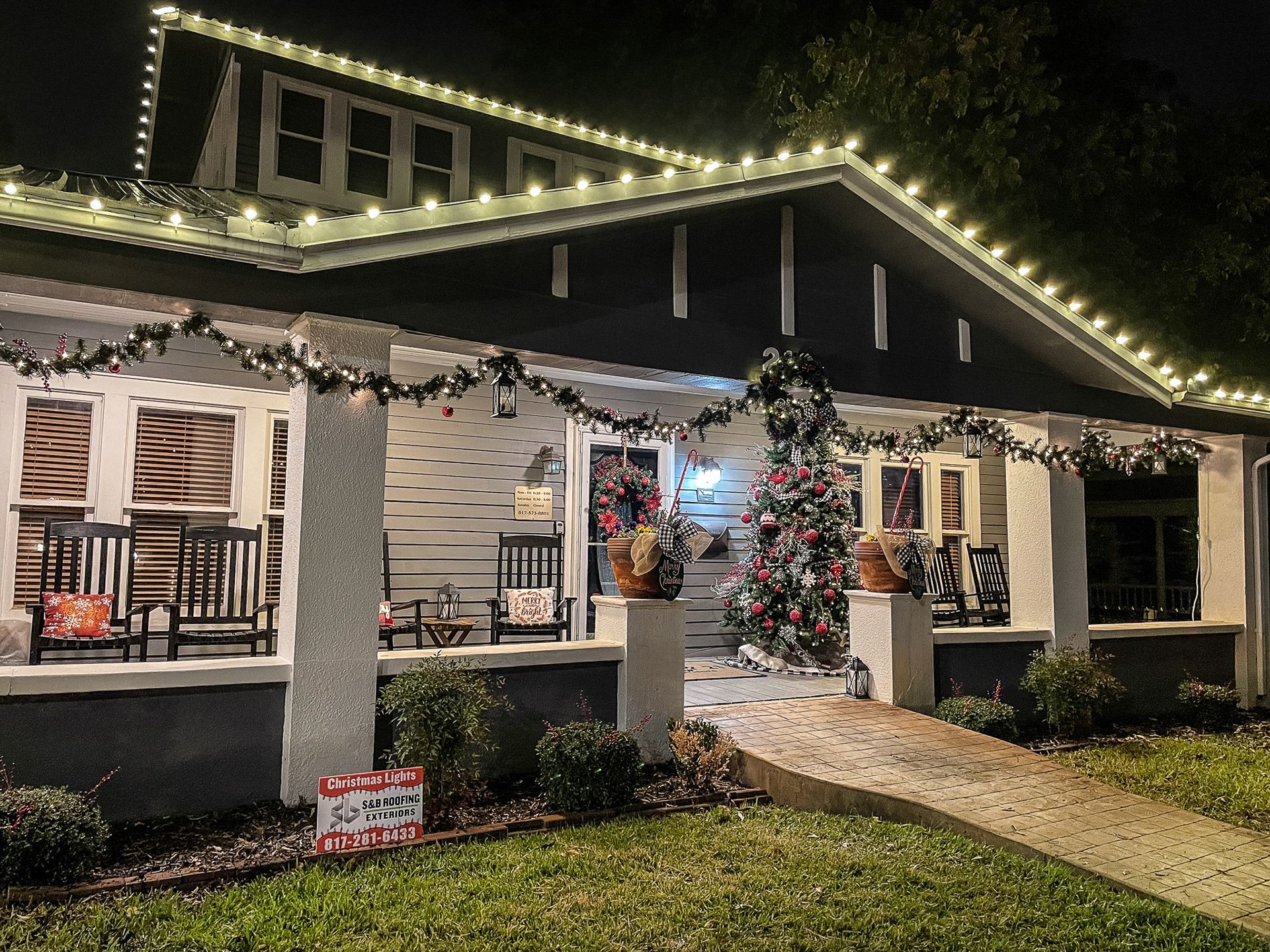 A house decorated with Christmas lights and garlands, with a tree on the porch.