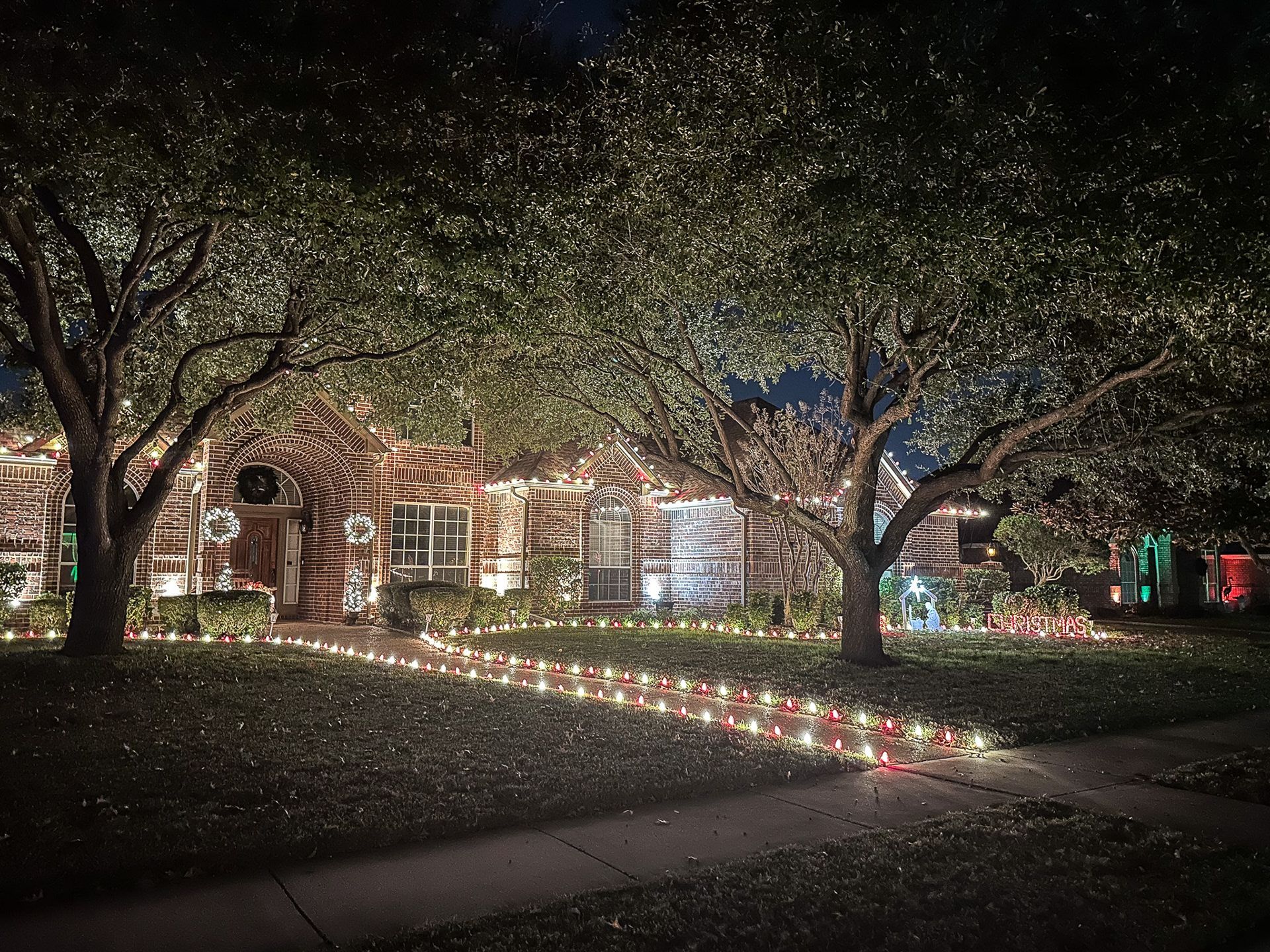 House decorated with Christmas lights at night; glowing pathway, trees, and facade.