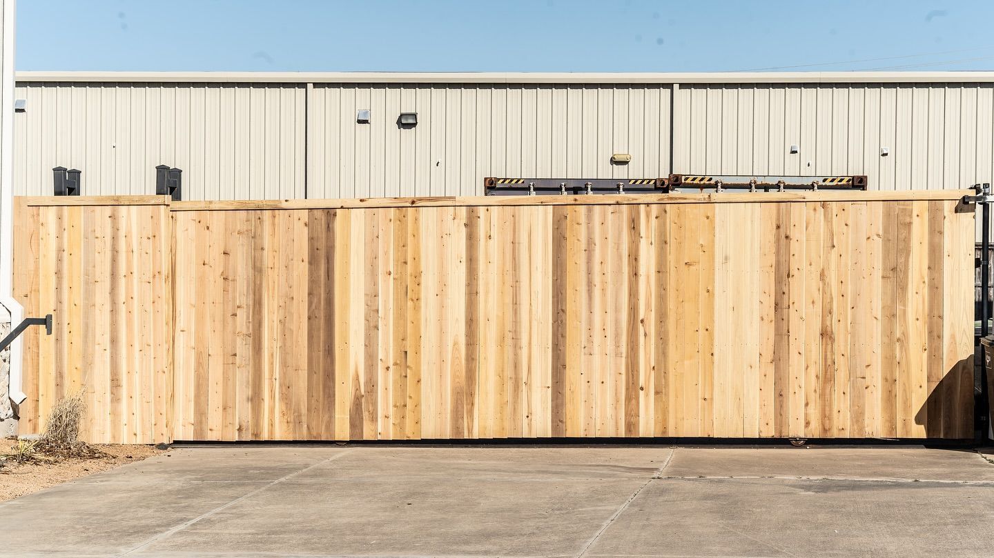 Wooden fence in front of a light-colored industrial building on a sunny day.