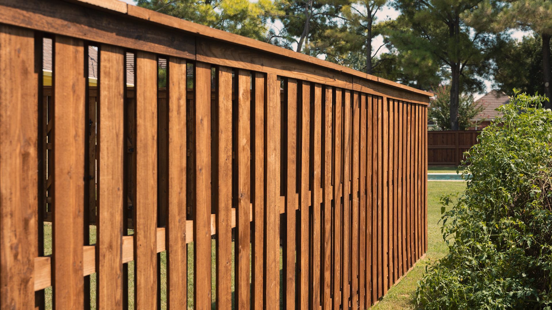Wooden fence in a yard with green grass and trees.