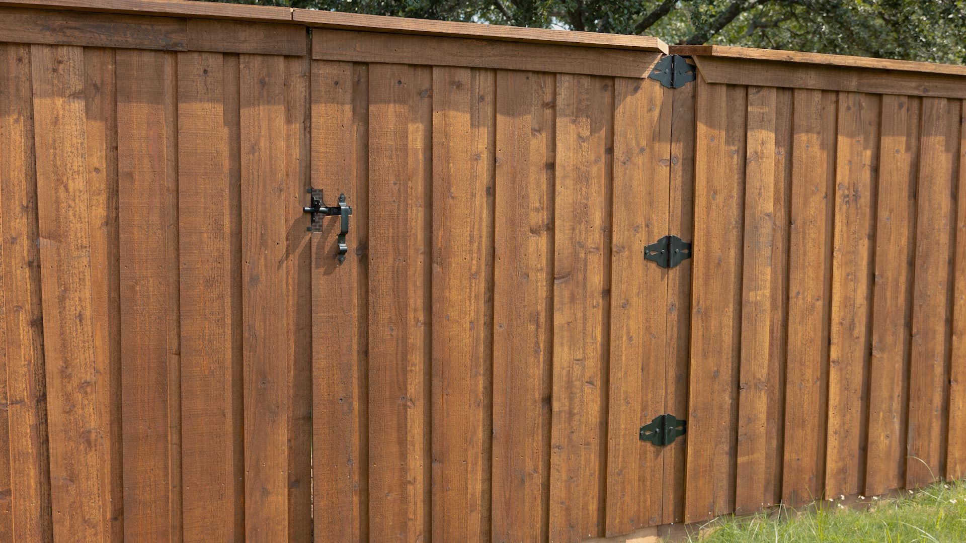 Wooden fence with a gate, stained brown. Metal hinges and handle.