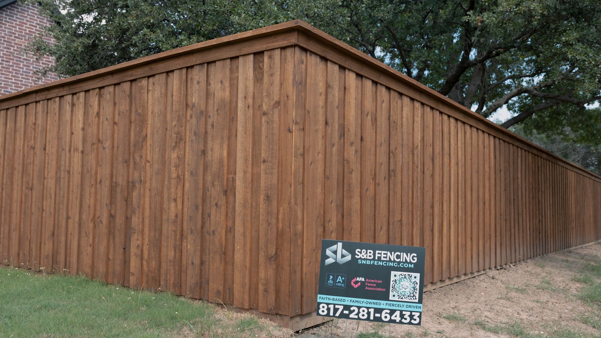 Brown wooden privacy fence in a yard, with a sign advertising fence company.