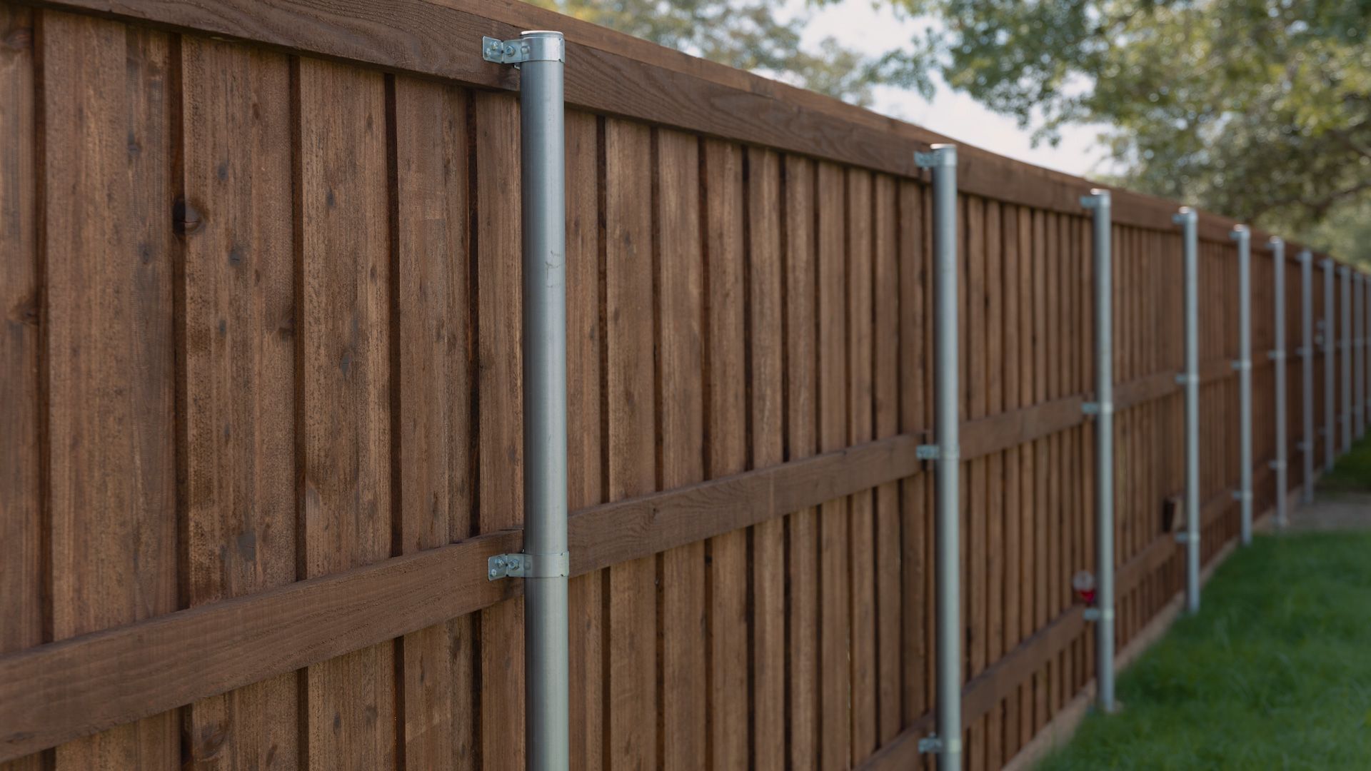 Wooden fence with metal posts along a green lawn, trees in the background.