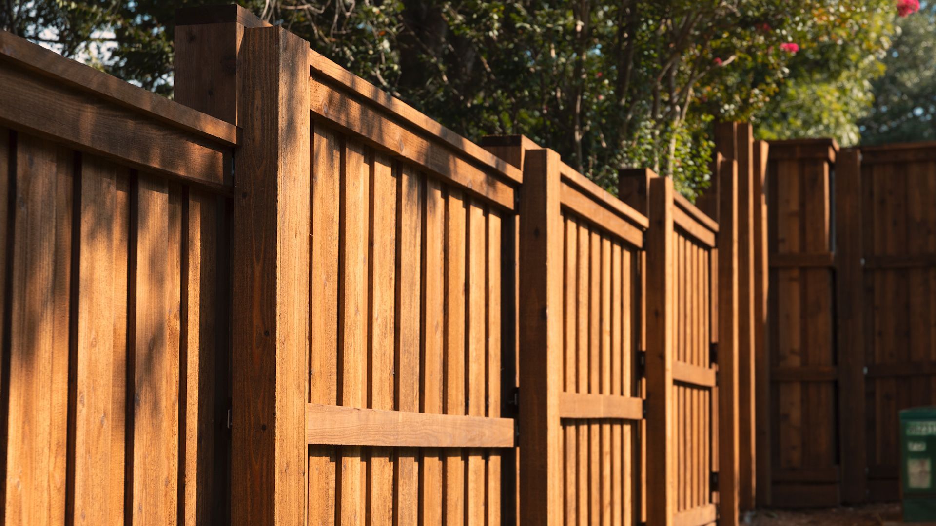 Wooden fence atop a stone wall in a backyard, with green grass and trees.