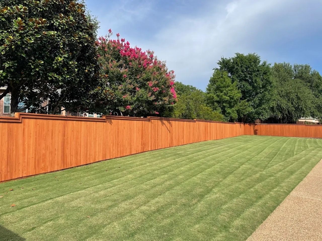 Wooden fence surrounding a green lawn under a bright blue sky.