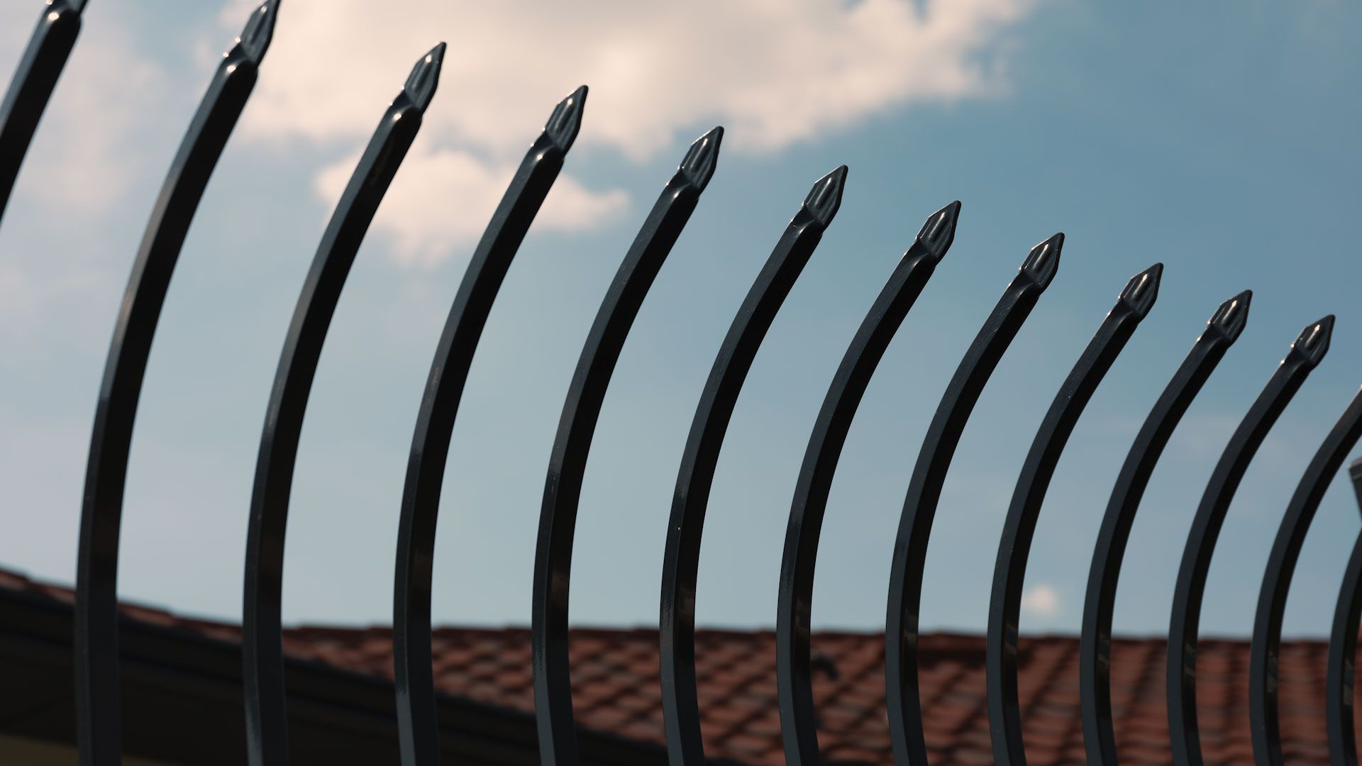 Black metal security fence with pointed tops against a blue sky.