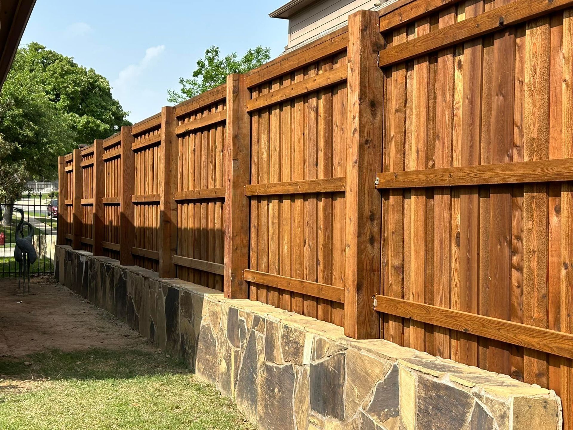 A wooden fence stained a warm brown color atop a stone retaining wall.