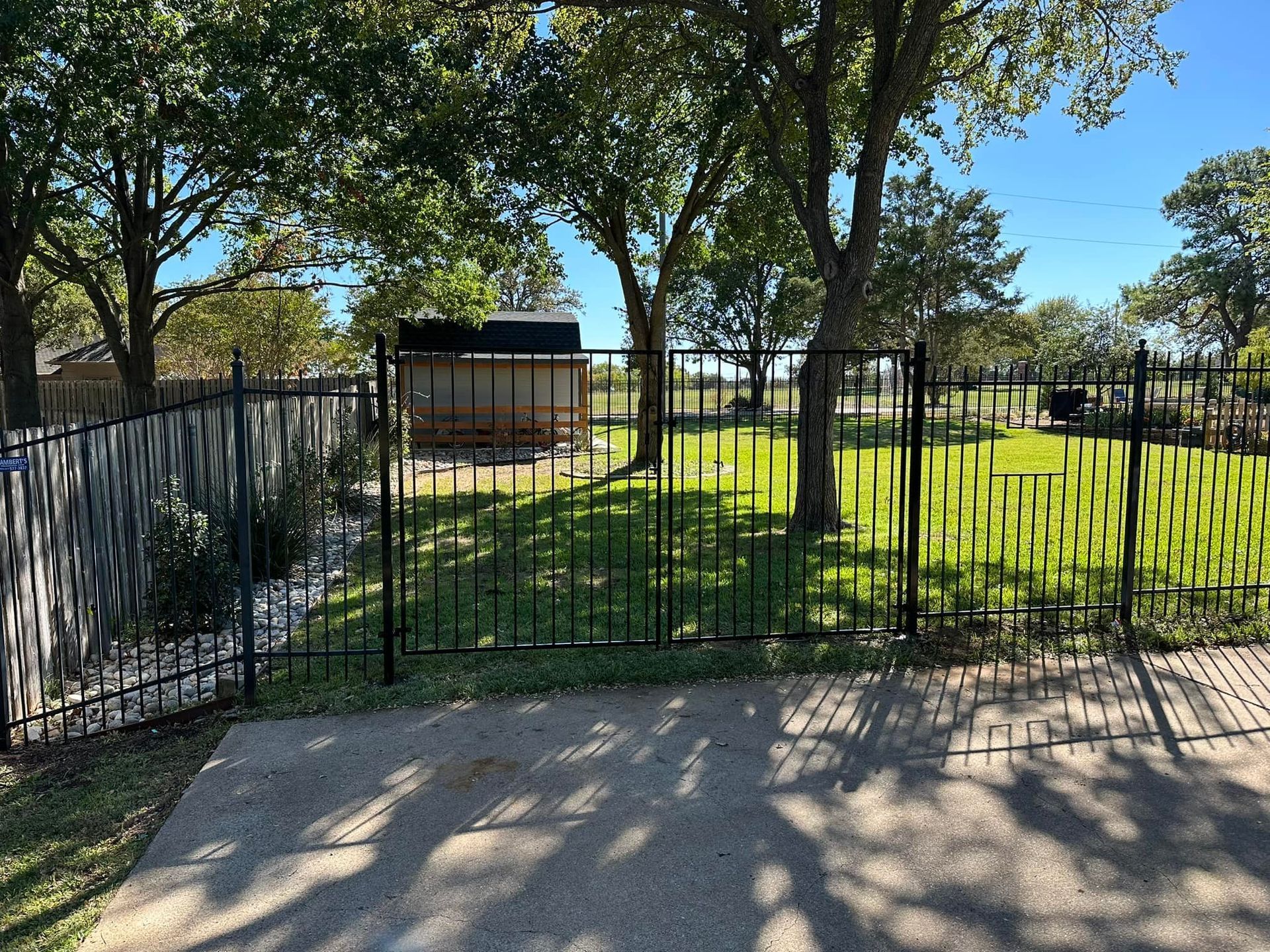 Black metal fence surrounding a grassy yard with trees under a bright blue sky.