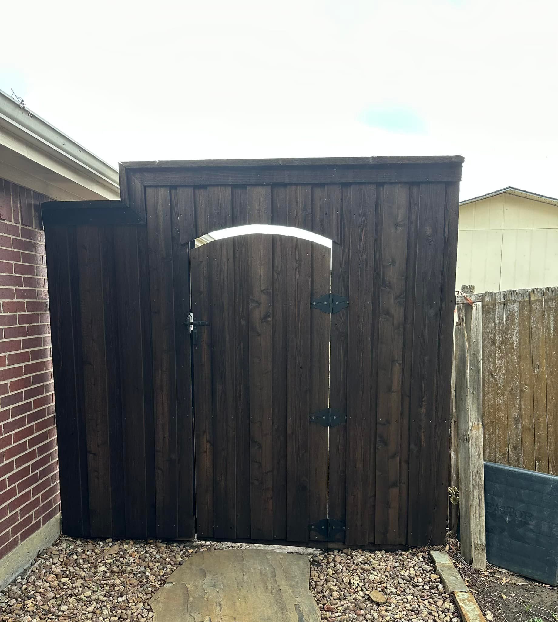 A dark stained wooden gate and surrounding fence, providing privacy next to a brick building.