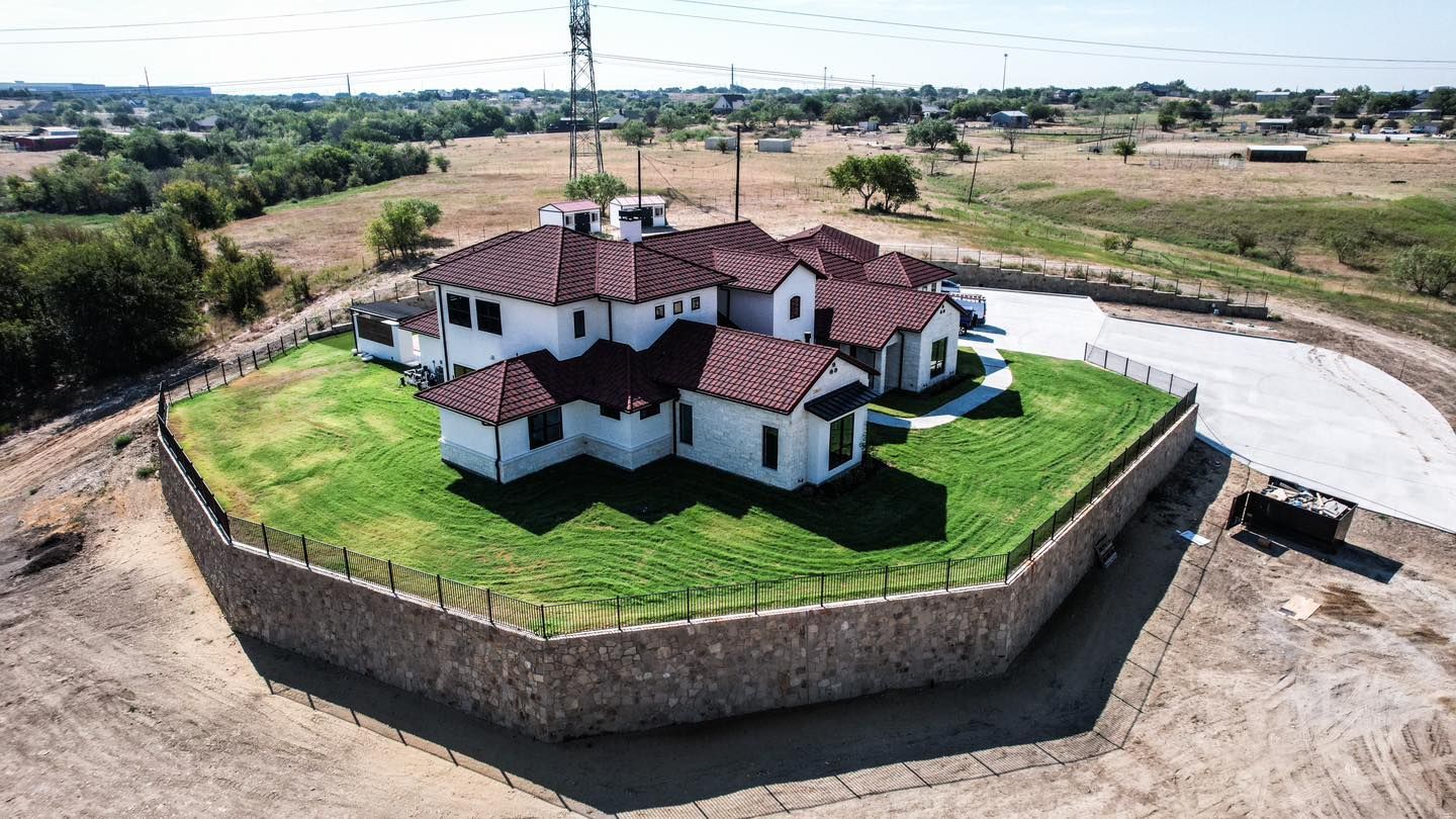 White house with a red tile roof sits atop a circular, grassy hill surrounded by a stone wall.