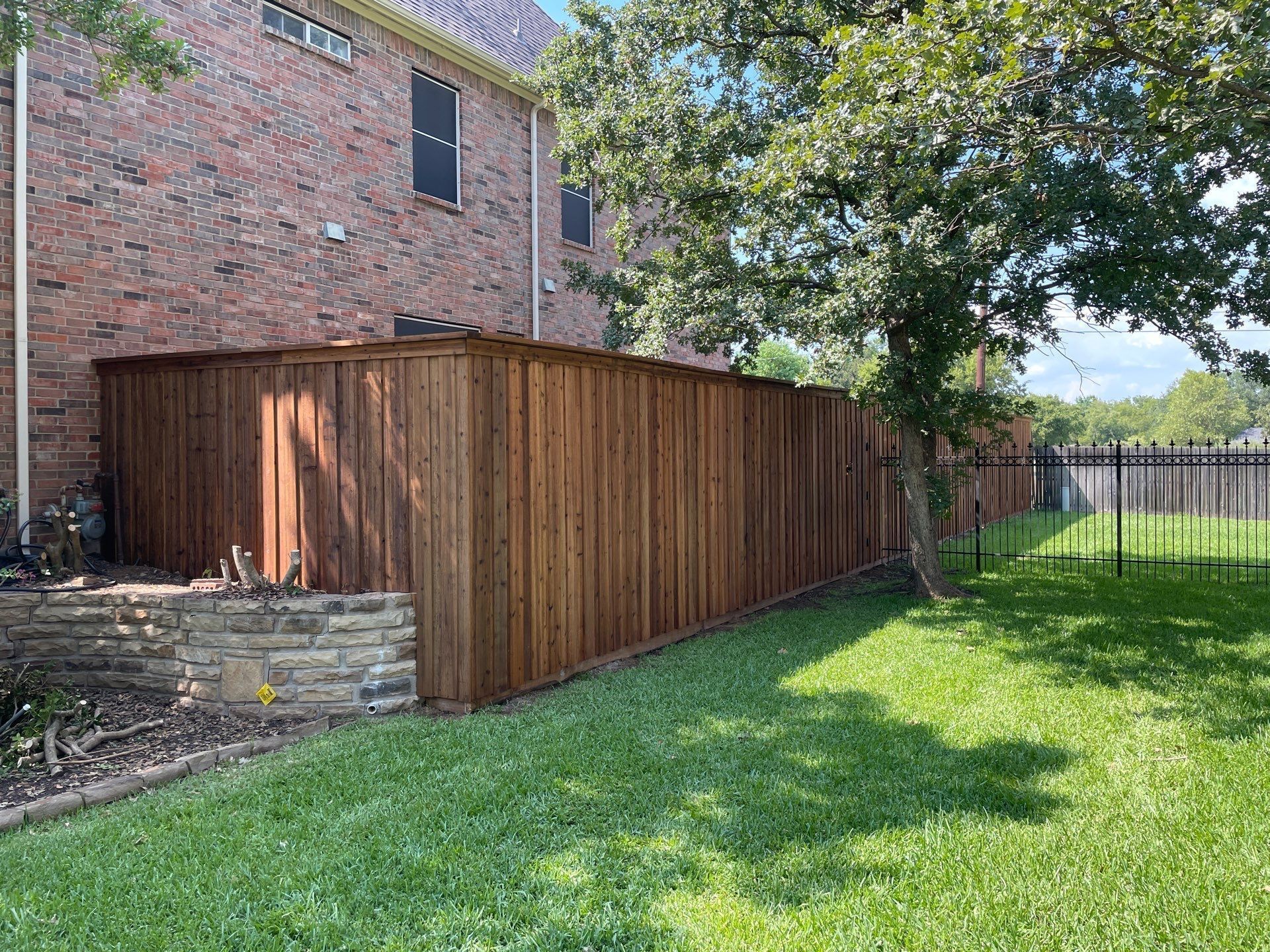 Brown wooden fence along a brick house and green lawn.