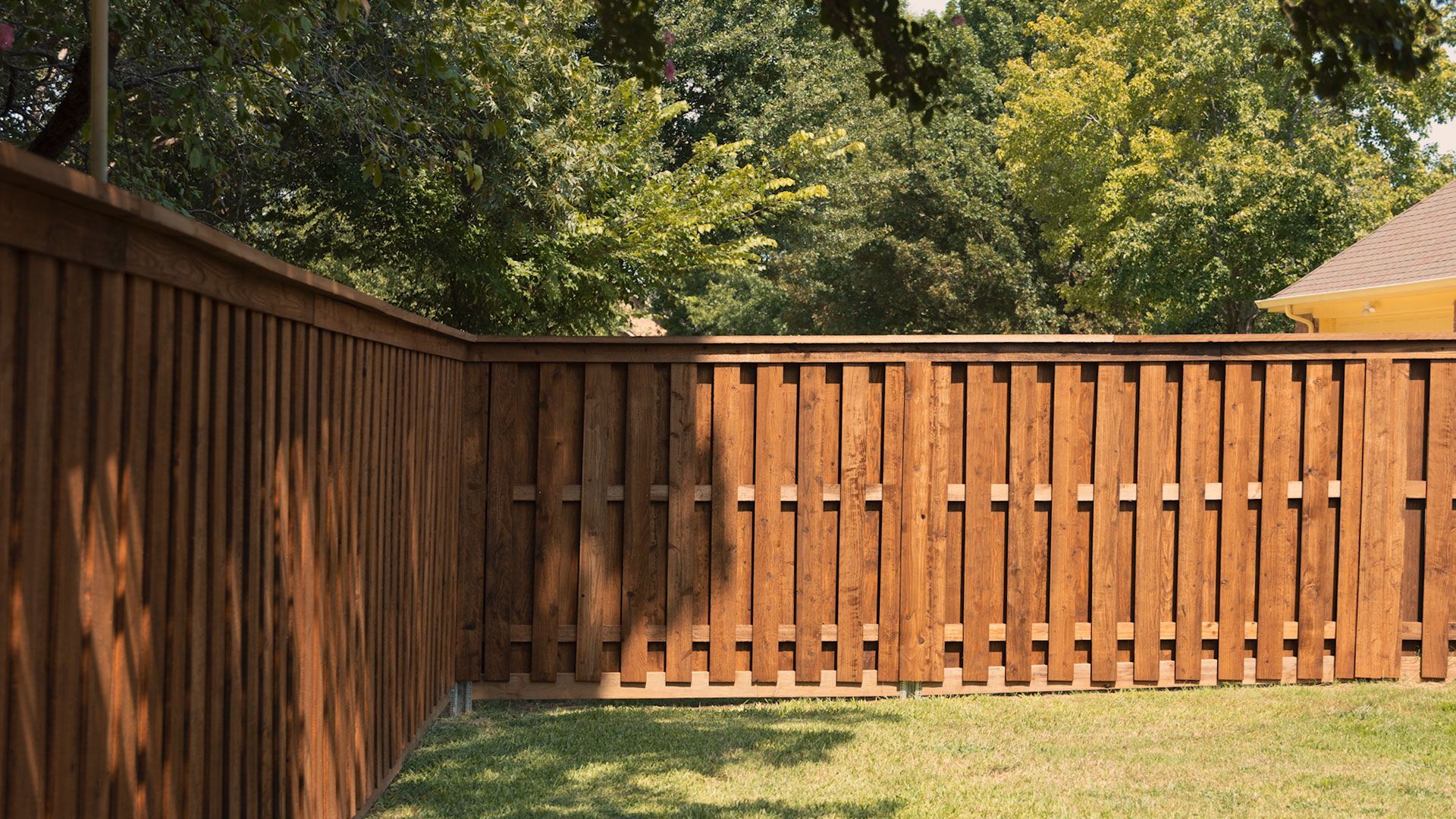 Wooden privacy fence in backyard with green grass and trees.