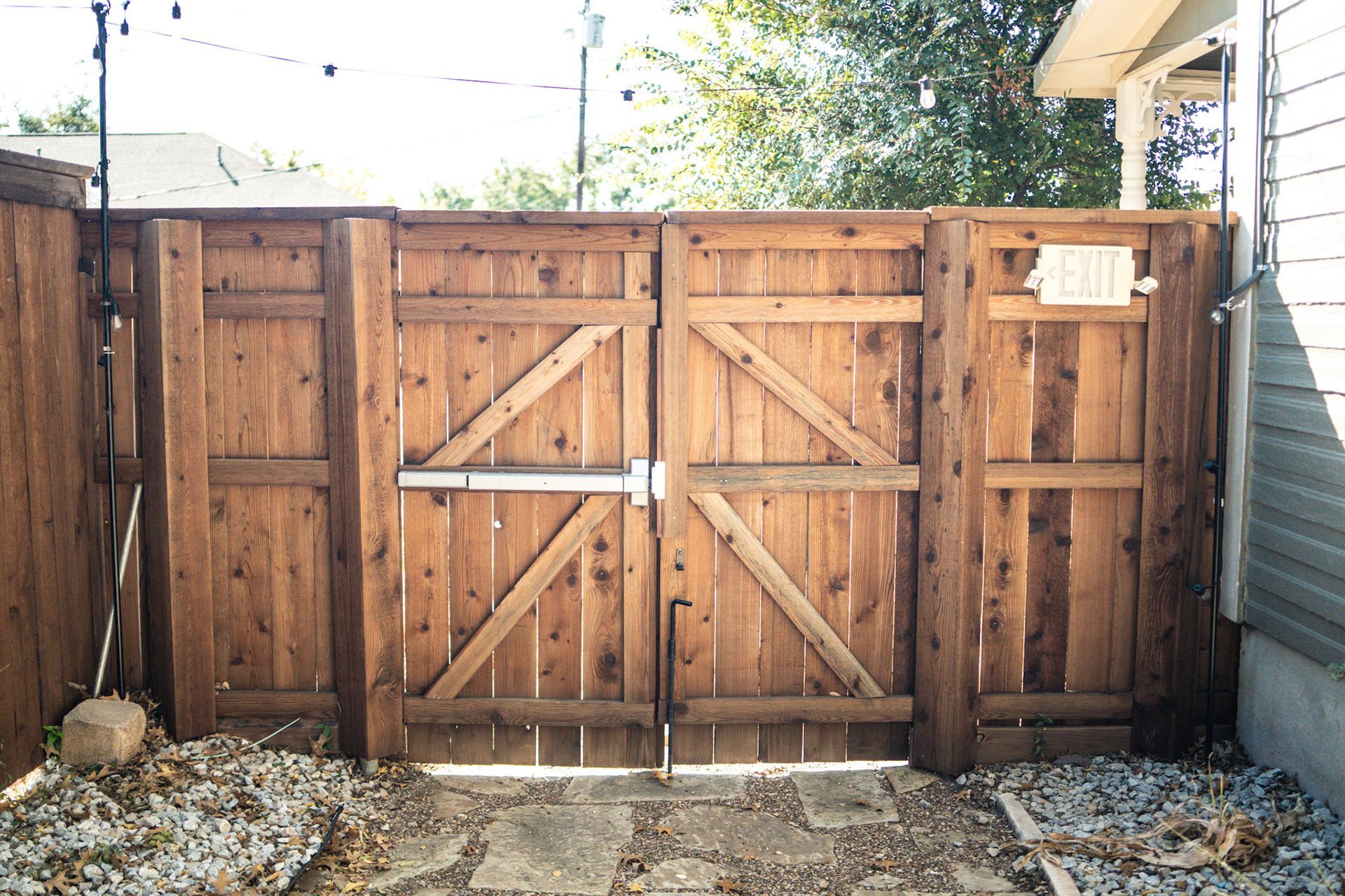 Wooden double gate in a backyard, with gravel ground and some leaves.