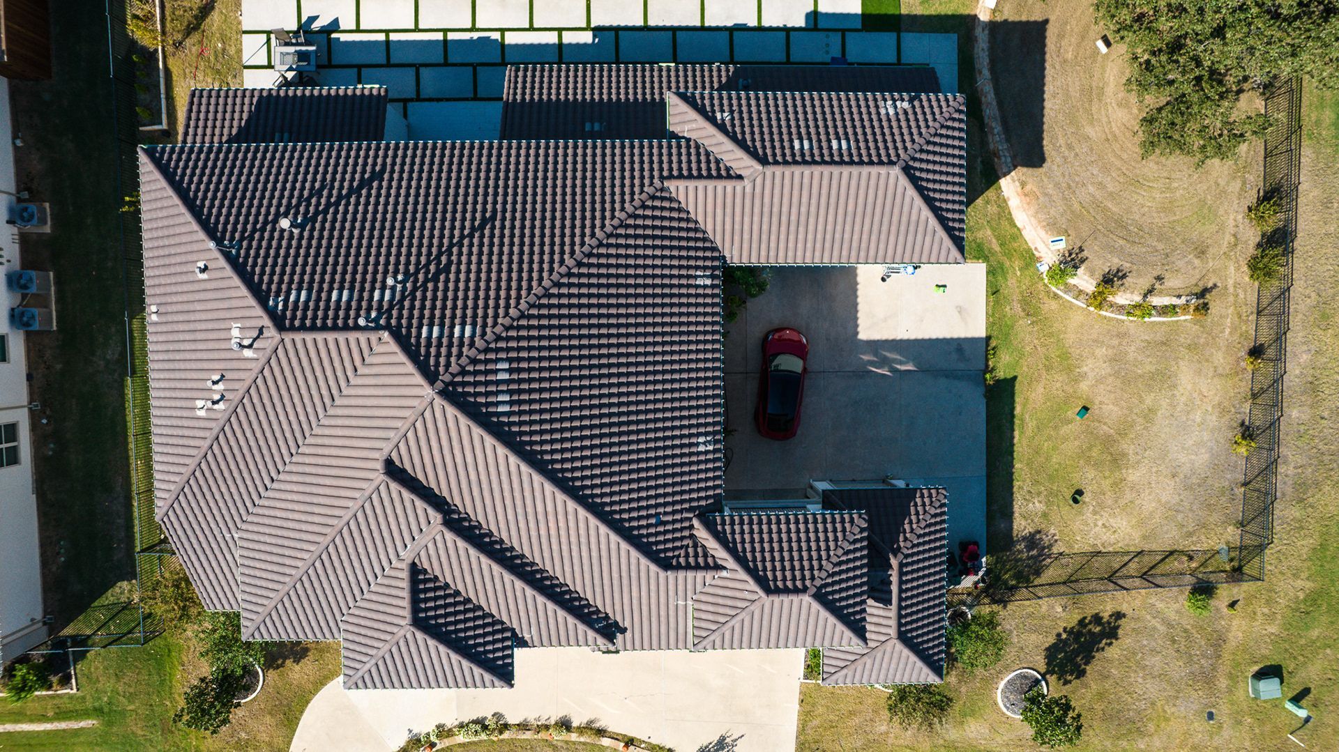 Aerial view of a modern home with a brown roof, a driveway with a car, and surrounding green lawn.