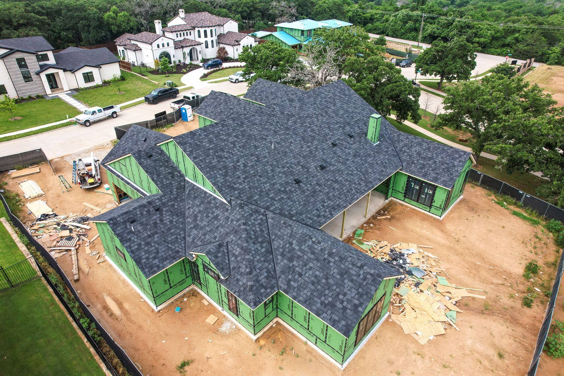 Newly constructed house with green wrap and dark roof in a suburban setting.