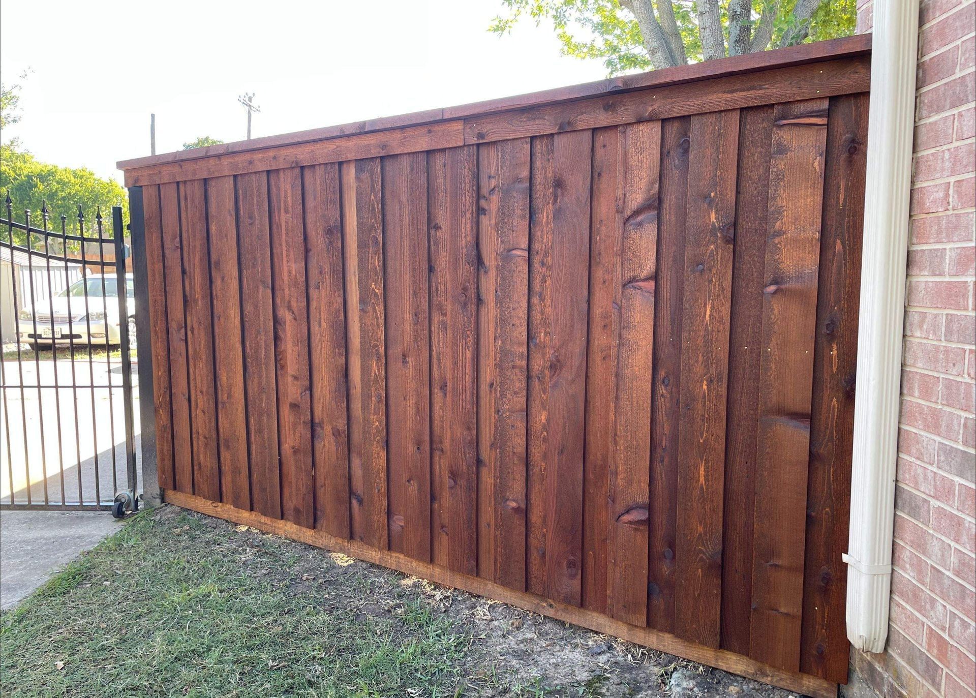 Wooden fence stained dark brown next to a brick wall and a wrought iron gate.