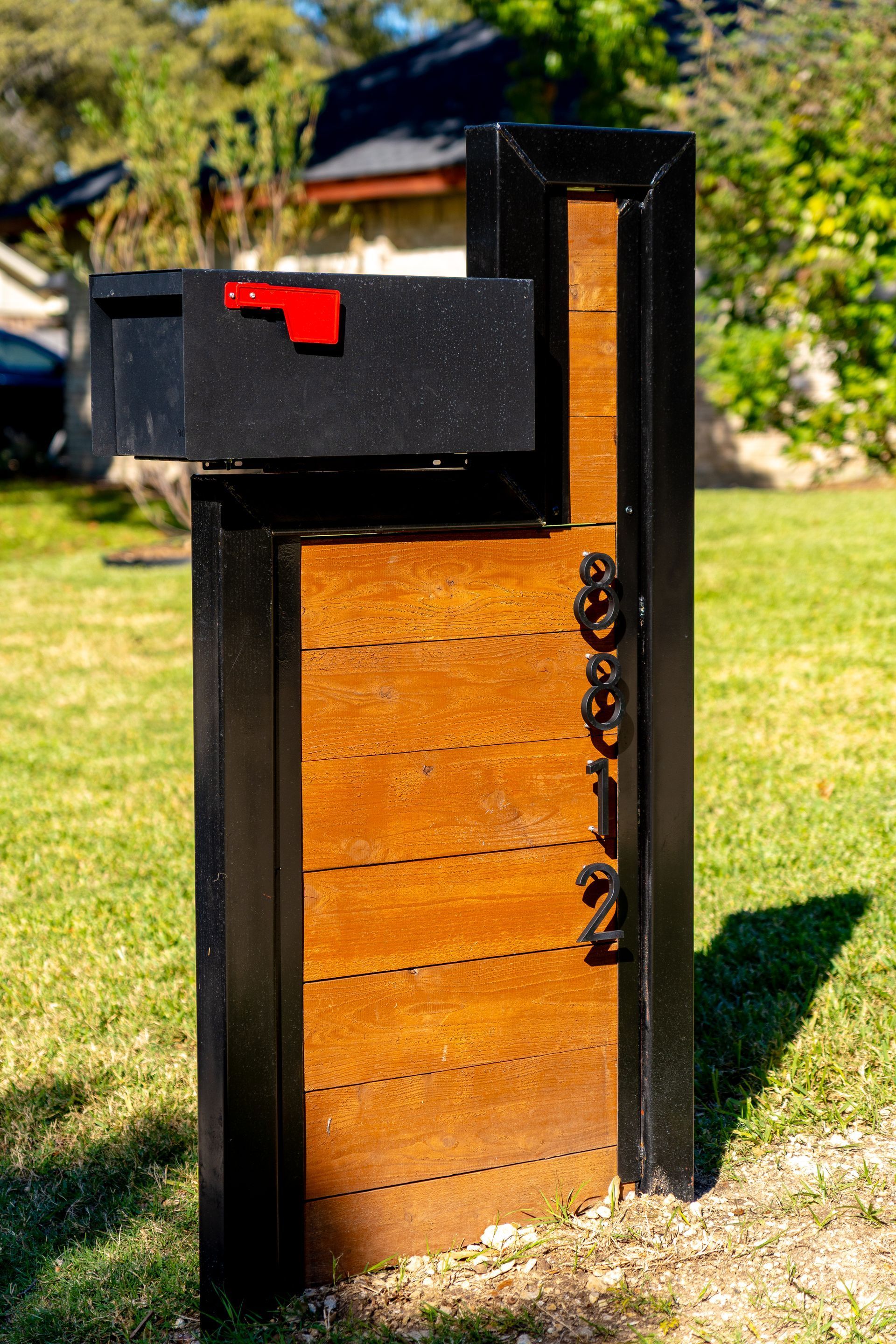 Black mailbox with red flag, mounted on a wooden and black post, with address 8612 in bronze.