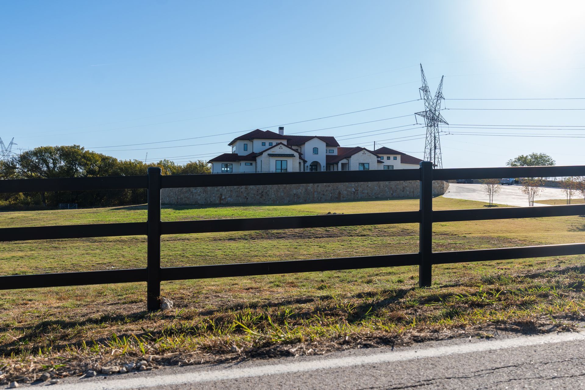 Black fence in front of a large, two-story house with a red tile roof on a grassy plot under a blue sky.