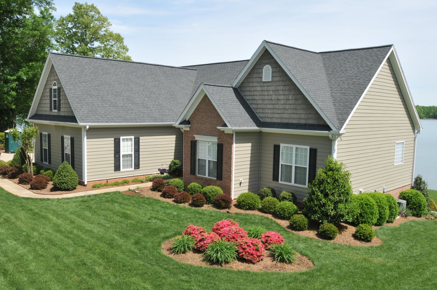 A large house with a gray roof is sitting next to a body of water.