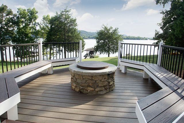 A wooden deck with a fire pit and benches overlooking a lake.
