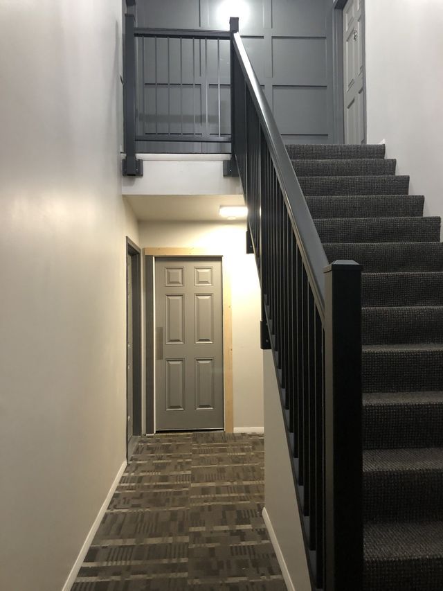 A hallway with stairs leading up to a door and a railing.