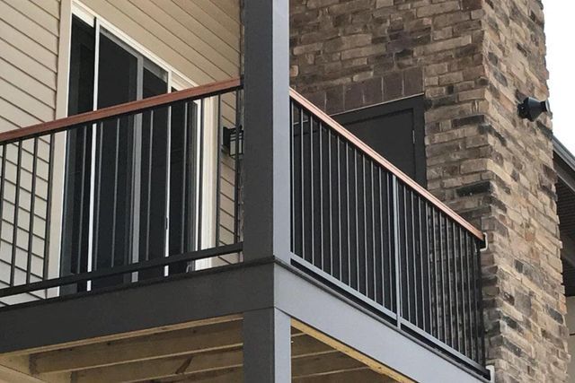 A balcony on the side of a brick building with a black railing.