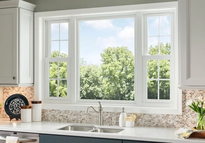 White kitchen window over a sink, with a view of green trees and a partly cloudy sky.