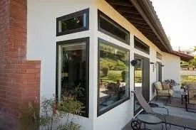 Exterior corner of a white stucco house with black-framed windows and a red brick wall.