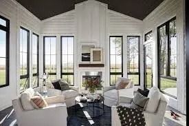 Sunroom with white walls, black framed windows, and white armchairs arranged around a coffee table.