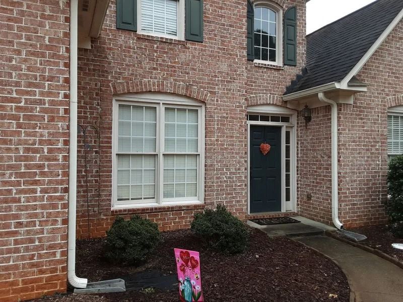 Brick house with dark green door and shutters, white trim, and a small yard with bushes.