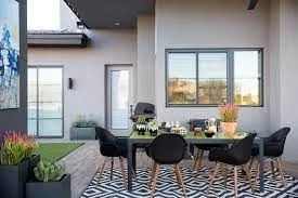 Outdoor dining space with black table, chairs, plants, and a patterned rug.