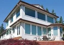 Two-story white house with large windows, set against a blue sky, and deck with seating.