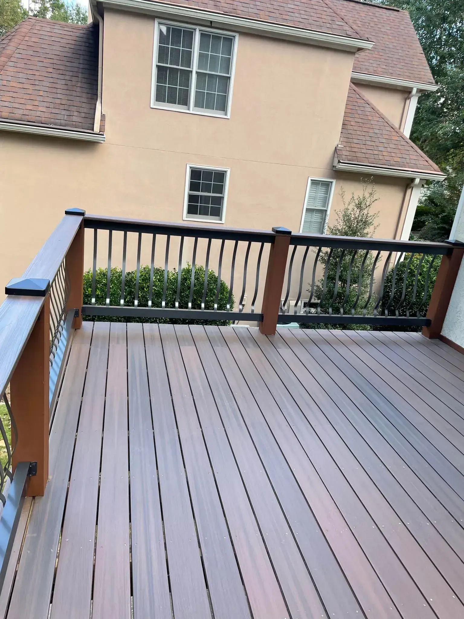 Wooden deck with black railing and brown house in the background.