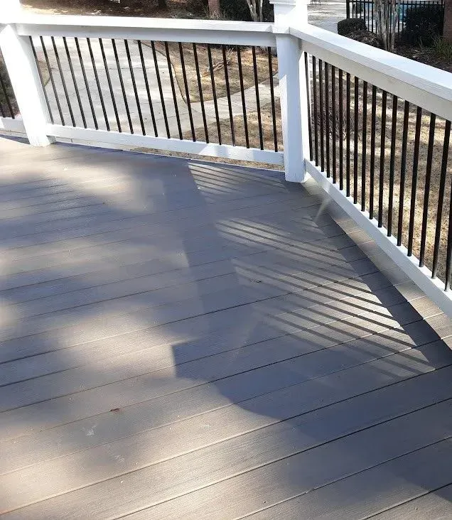 Gray composite deck with white railing and black spindles, sunny outdoors.