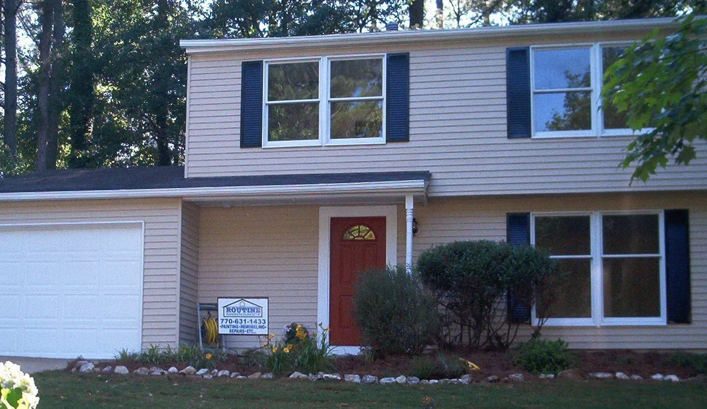 Two-story house with beige siding, black shutters, white garage door, and red front door.