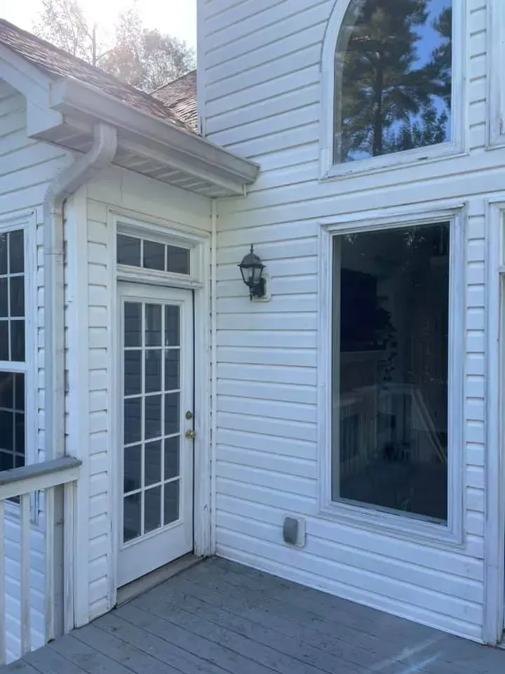 White house exterior with door, windows, and light fixture on a deck.