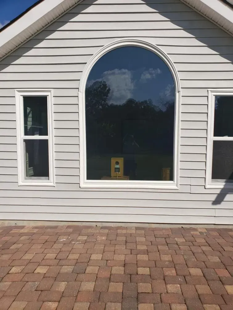 Gray house with arched and rectangular windows; brick patio in foreground.