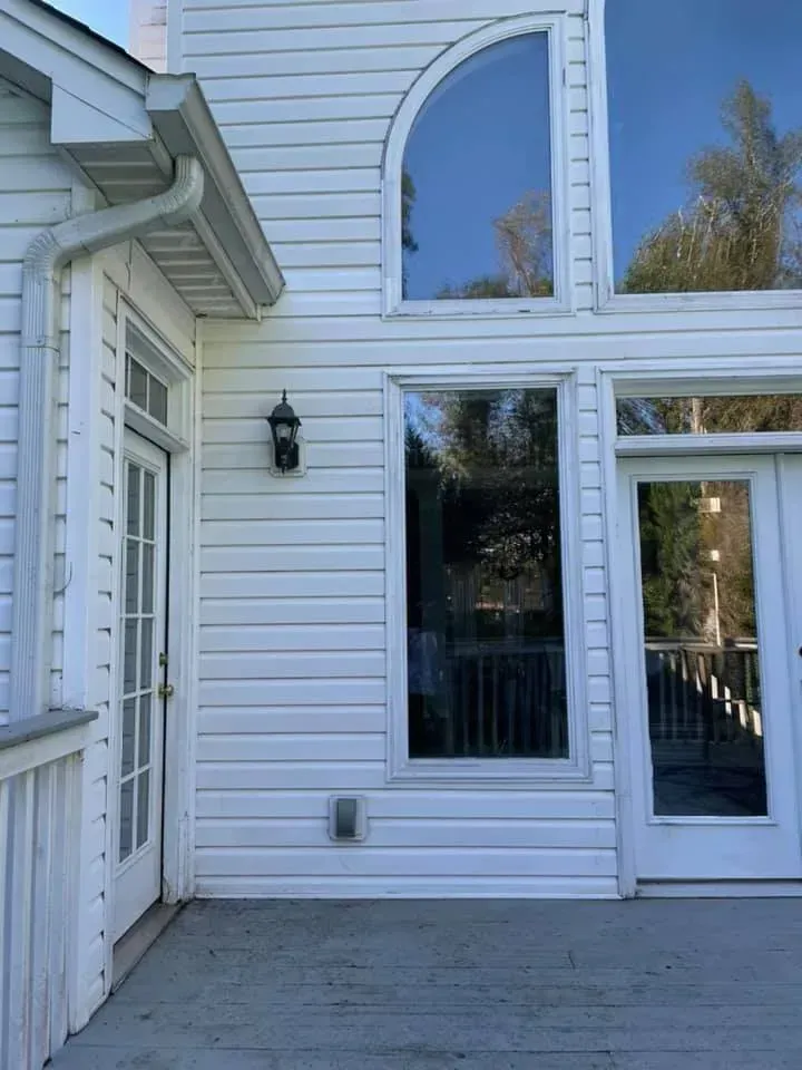 White house exterior with tall windows, a deck, and a door.