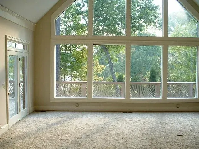 Empty room with large windows overlooking a green landscape. Beige walls, carpet.