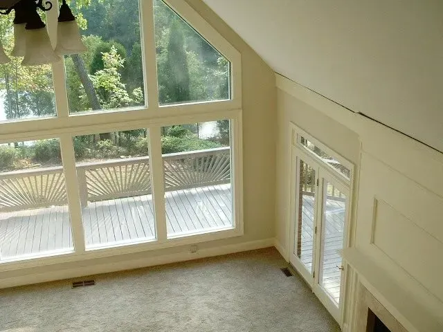 Large windows and a door overlooking a deck. Interior, light-colored walls, carpet.